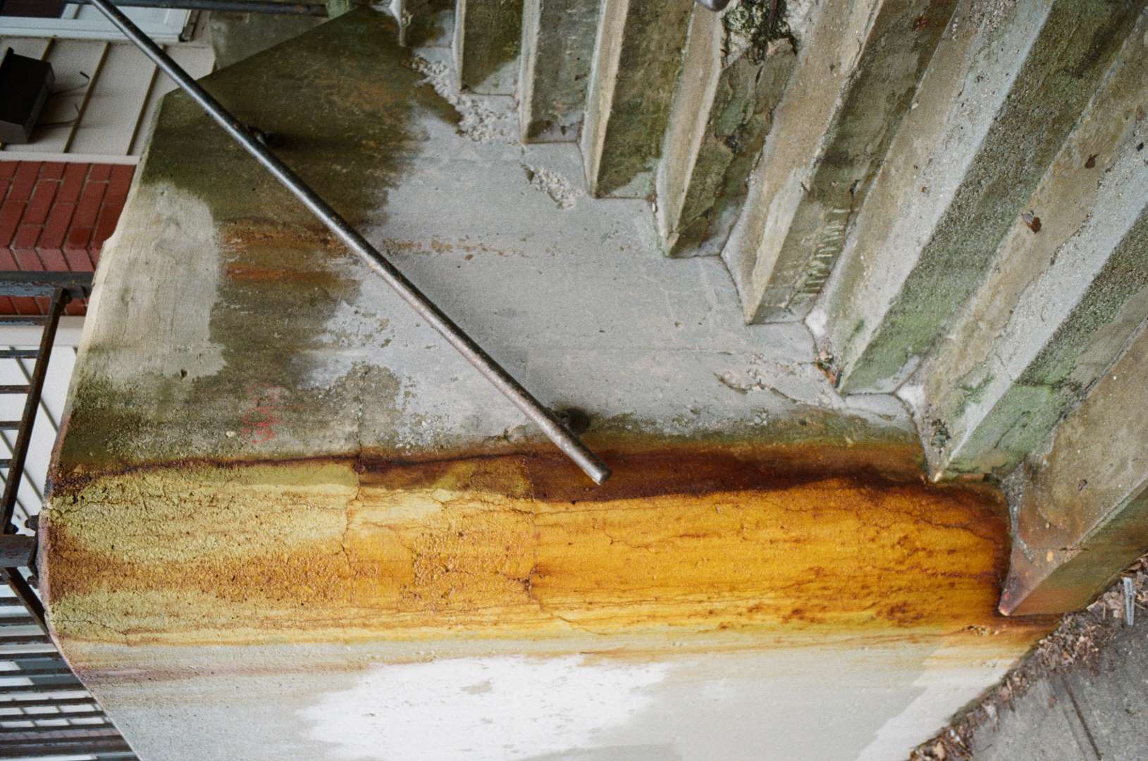 A colour photograph of a cracked and rust stained wall and stairs.