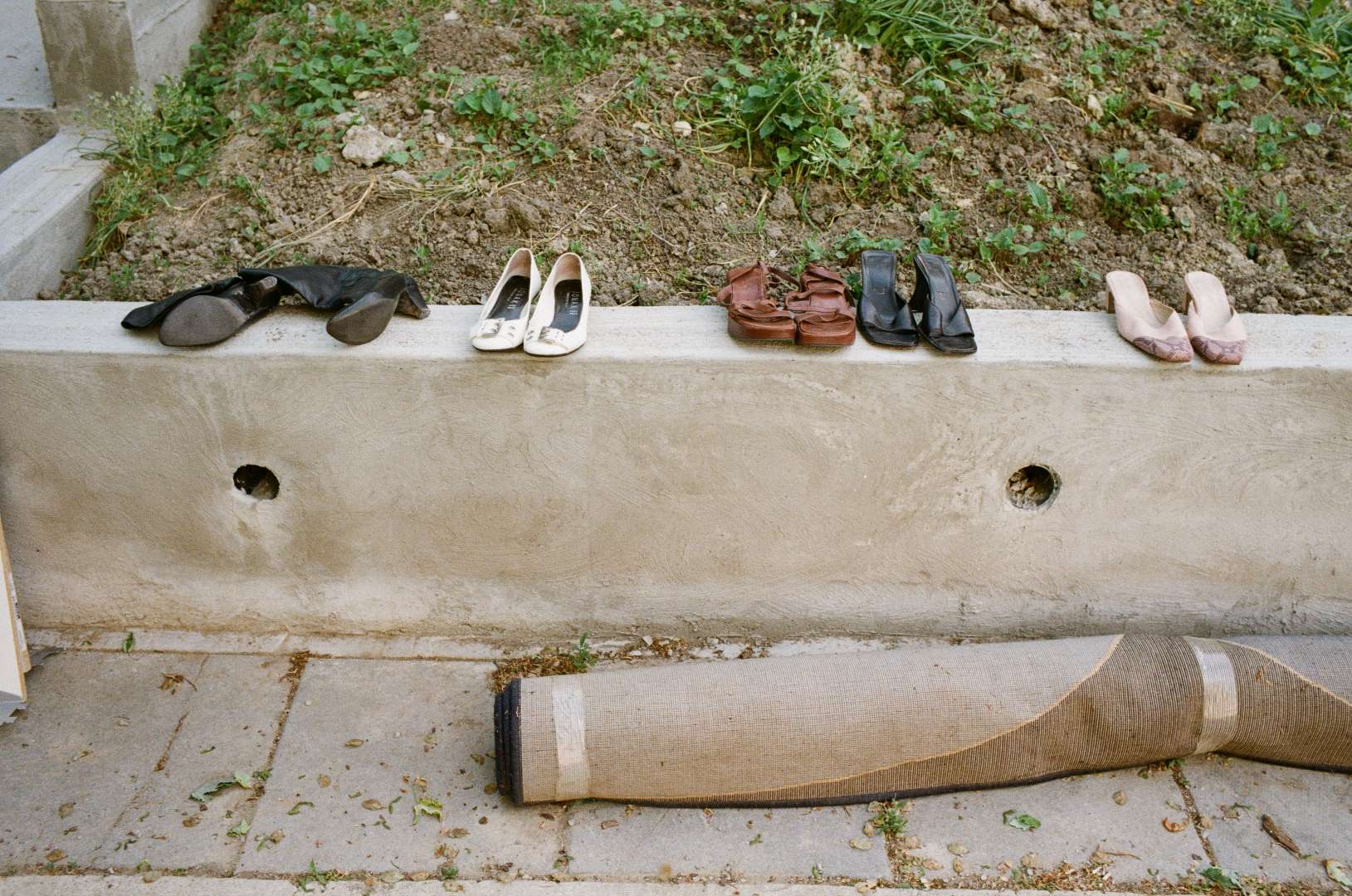A colour photograph of used shoes and a rug left on the sidewalk