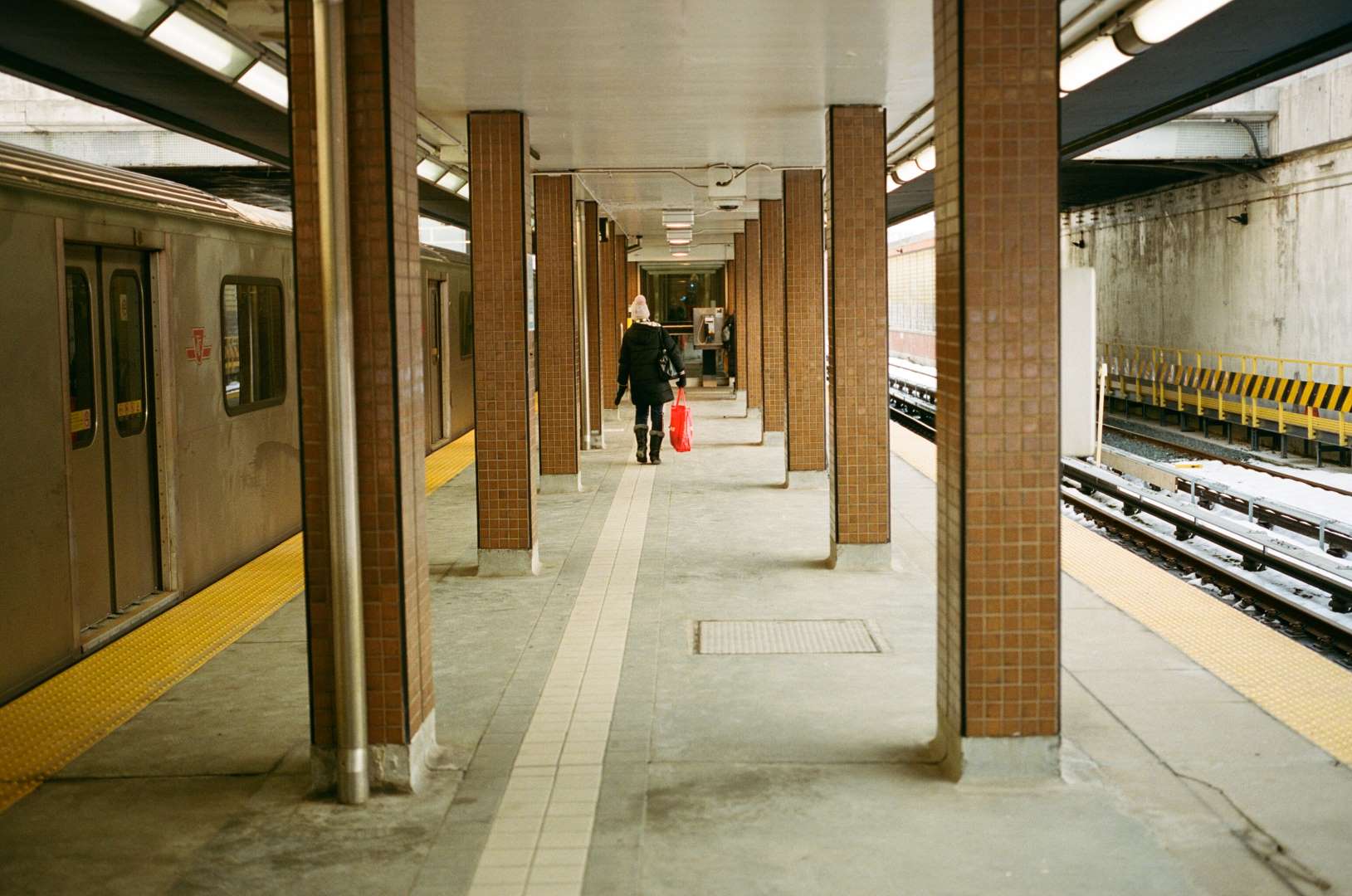 A colour photograph of a subway platform, a woman walks away towards the exit.