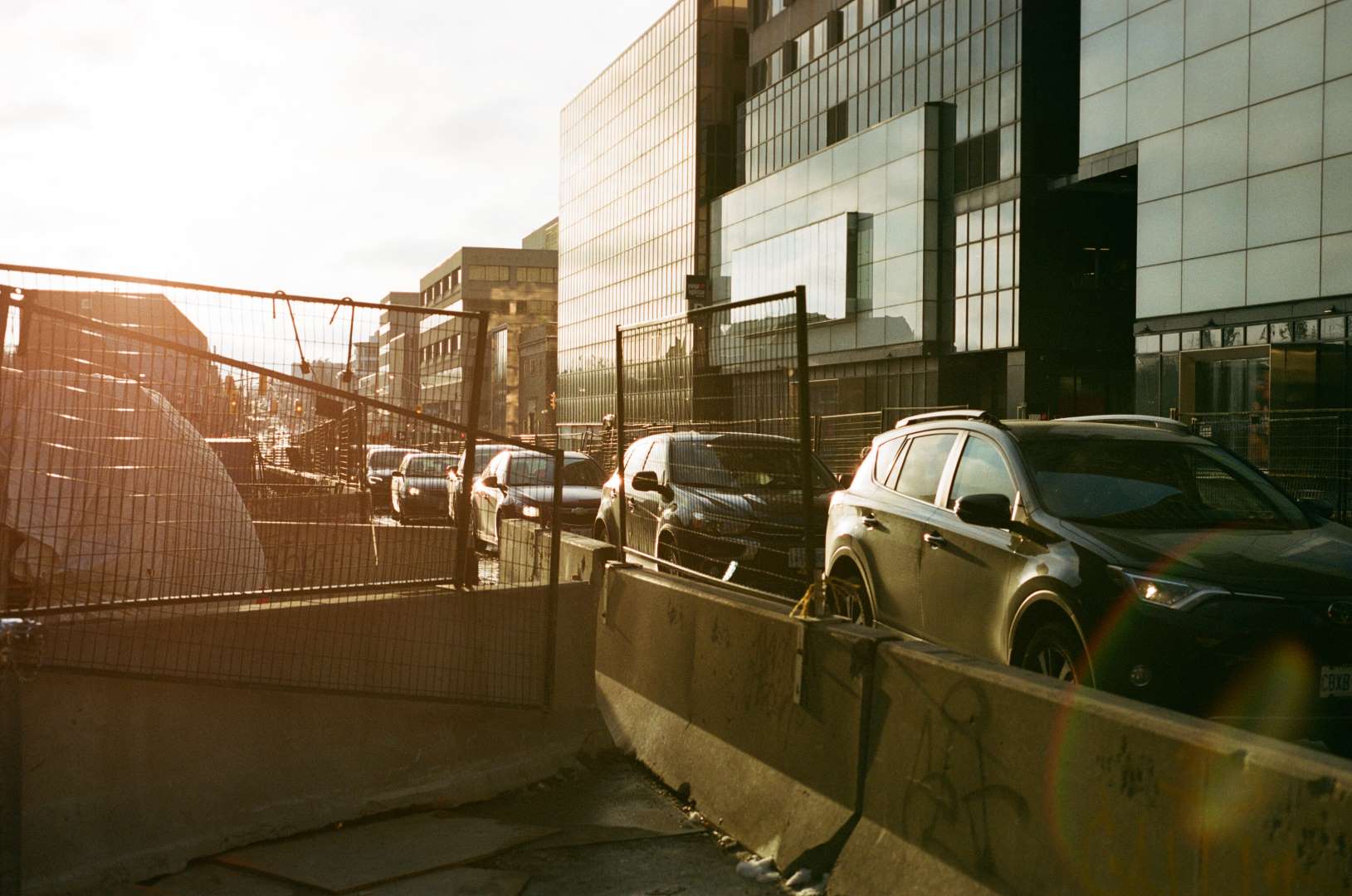 A colour photograph of cars in traffic as the sun sets, a rainbow flair is promenently visible