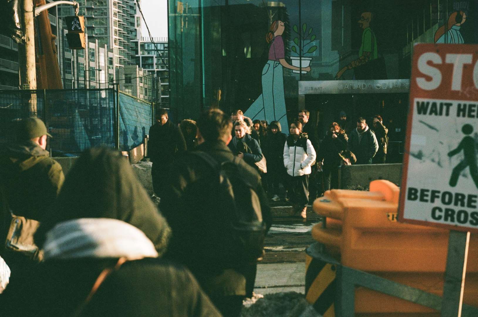 A colour photograph of a crowd of people waiting to cross the street with the sun strongly illuminating them from the side