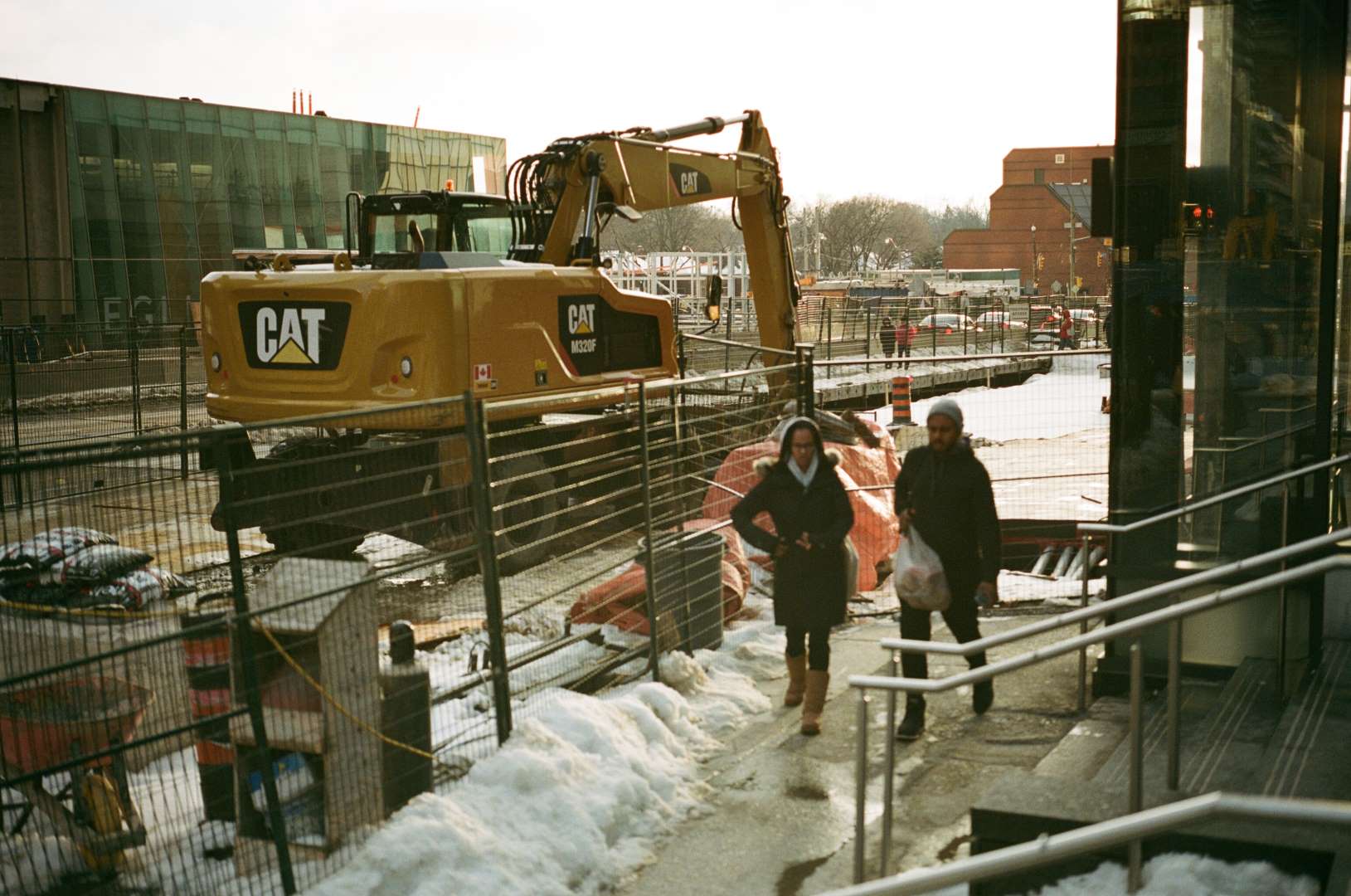 A colour photograph of two women walking next to a large earth excavator
