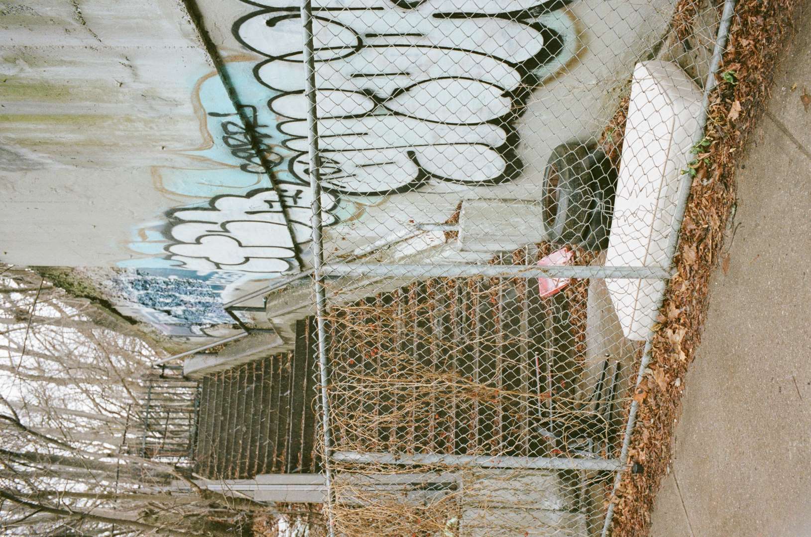 A colour photograph of an exterior stairwell, fenced off with a mattress and chair behind it