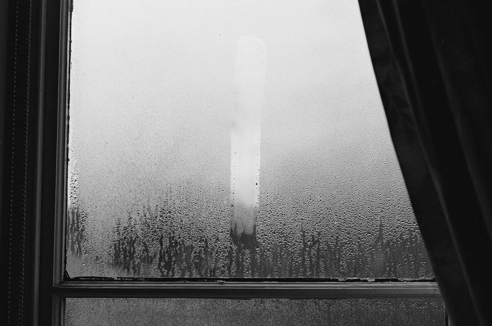 A black & white photograph of a foggy window with the letter I drawn on it