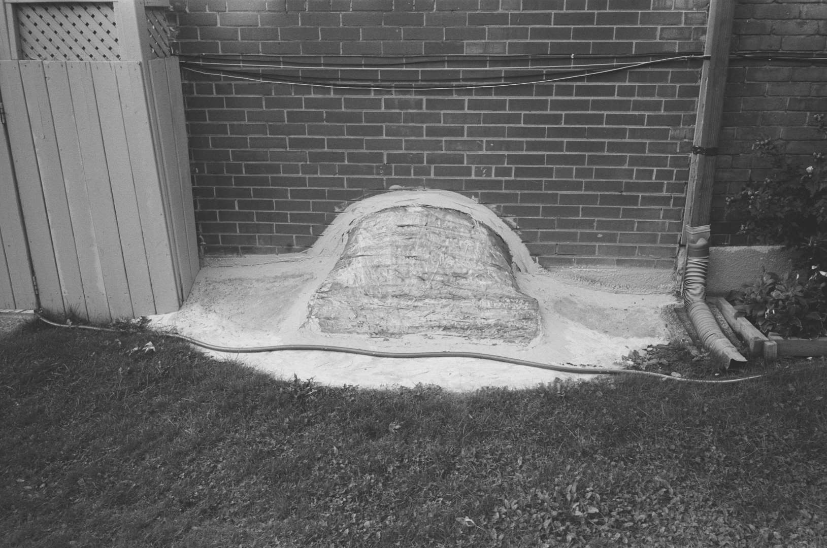 A black & white photograph of a ground level window will covered with clear sealing tape, something hidden in the basement?