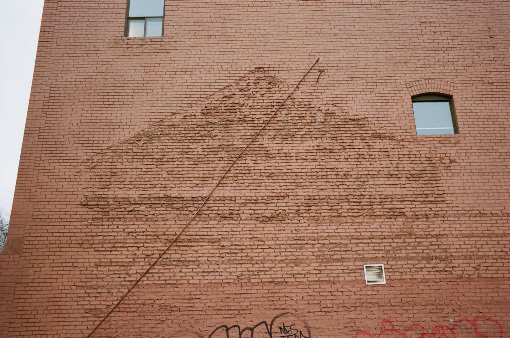 A colour photograph of a brick wall, the phantom of the house that used to touch the wall is visable through the difference in texture