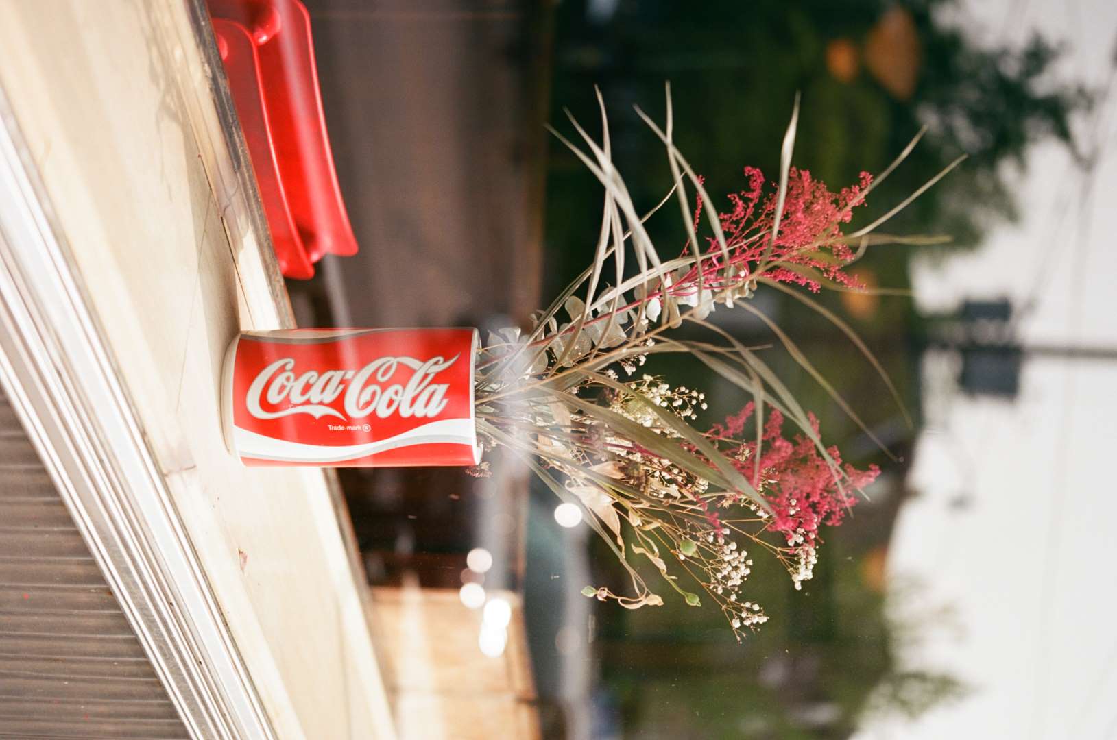 A colour photograph of a display of dried flowers in a Coca-Cola vase. There is an air of nostalgia and reflection.