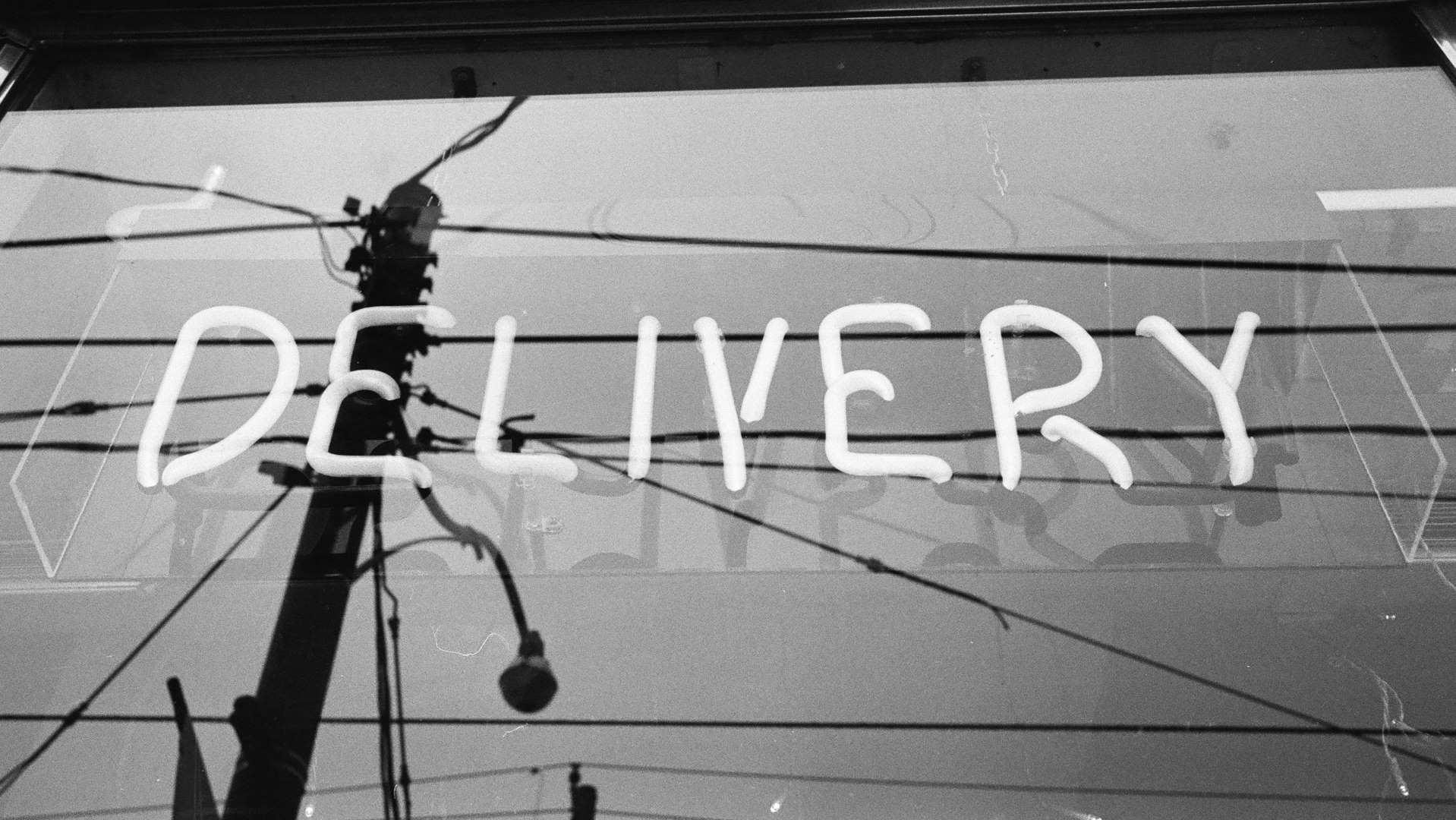 A black and white photograph of a neon sign 'DELIVERY'. There is an air of nostalgia and reflection.