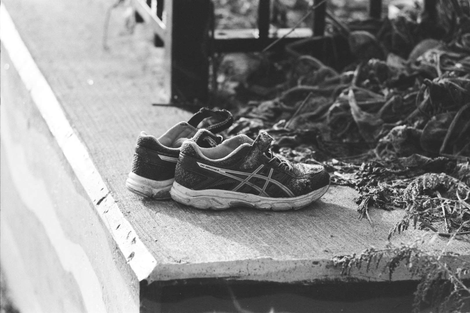 A black and white photograph of worn out running shoes left on a small wall
